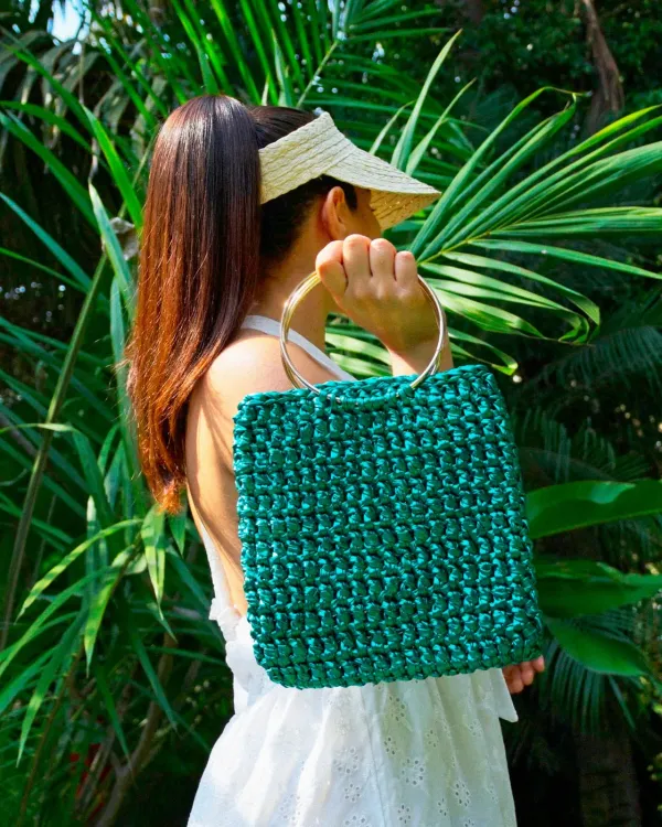Bolso tejido verde de Morain Atelier entre palmas.